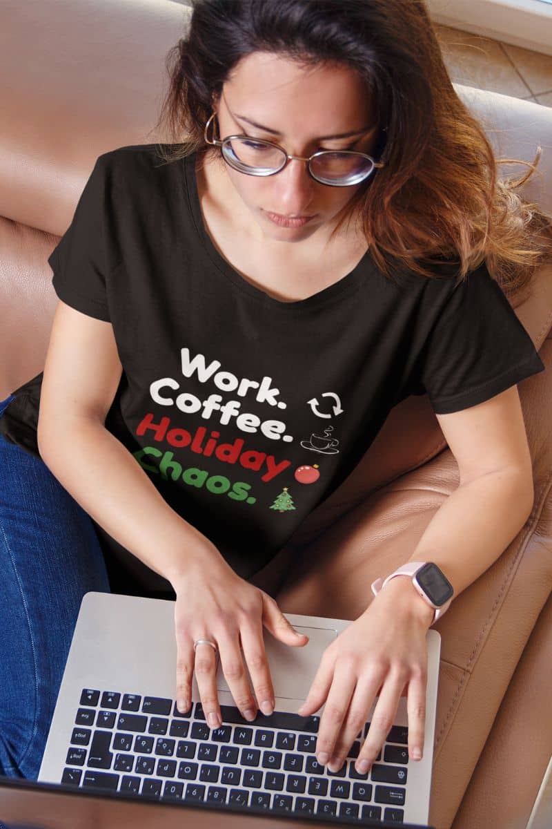 christmas shirt for coworkers with a  woman wearing a black t-shirt with text 'Work. Coffee. Holiday Chaos.' while using a laptop.