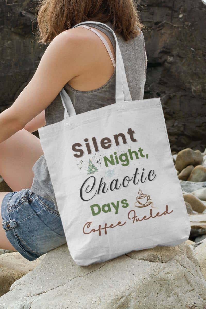 christmas shopper tote with a person sitting on rocks with a tote bag featuring humorous text 'Silent Night, Chaotic Days, Coffee Fueled'