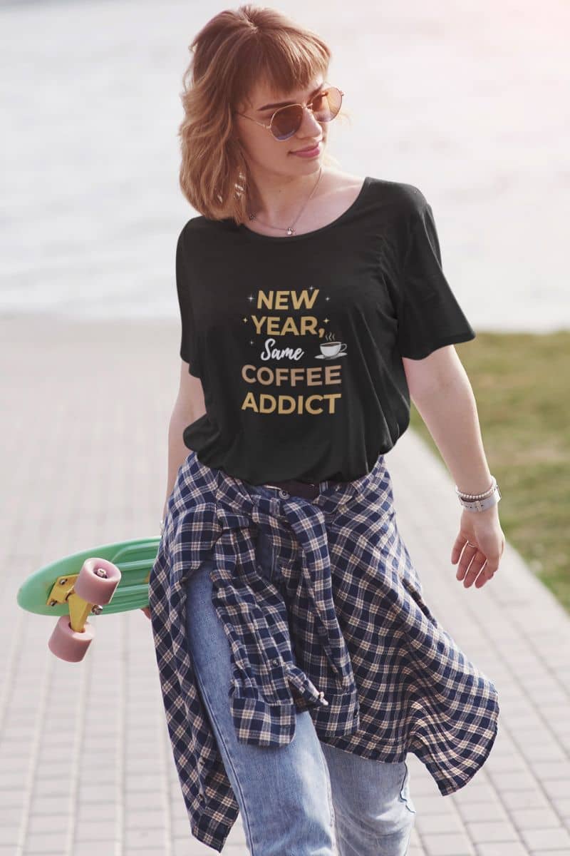 coffee lover gift shirt with a woman wearing a black t-shirt with text 'New Year, Same Coffee Addict', sunglasses, and a skateboard on a path.