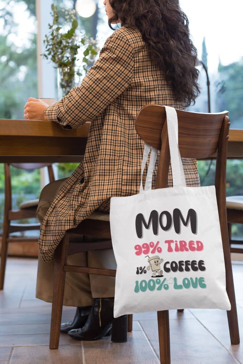 coffee lover mom tote bag with a person sitting at a table with a tote bag featuring a humorous mom quote.