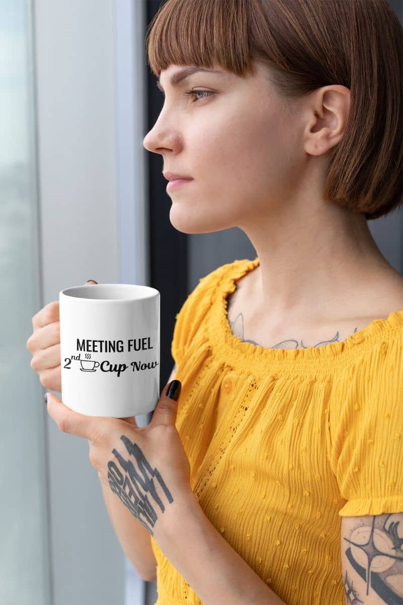 coffee lover mug with a woman holding a mug with text 'Meeting Fuel: 2nd Cup Now', wearing a yellow top indoors.