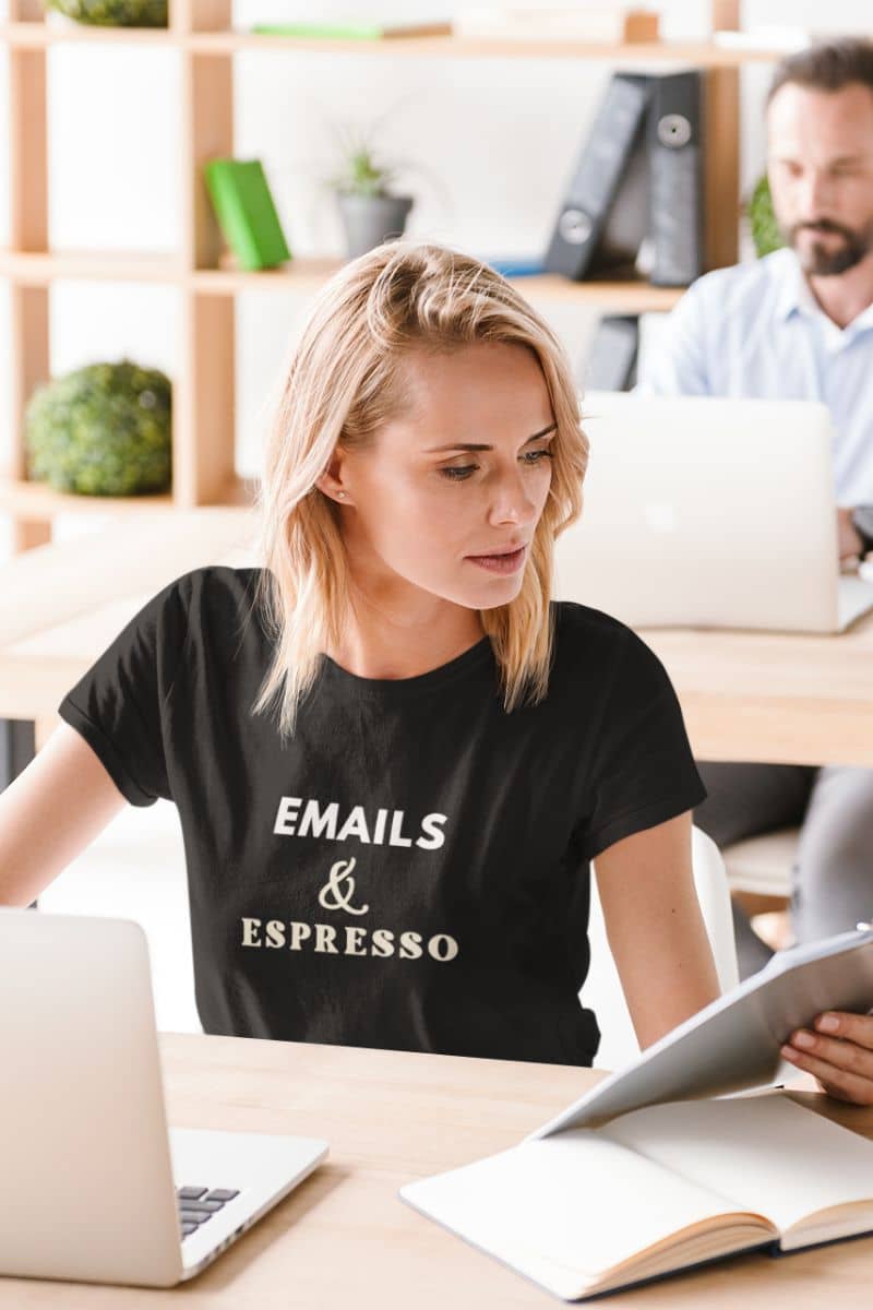 coffee lover shirt with a woman in an office setting wearing a black t-shirt with text 'EMAILS & ESPRESSO'.