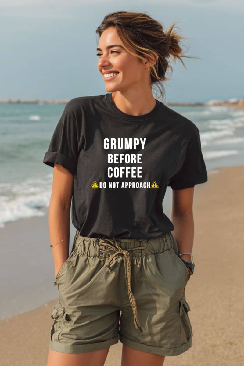 coffee lover shirt with a woman wearing a black t-shirt with text 'Grumpy before coffee, do not approach' on the beach