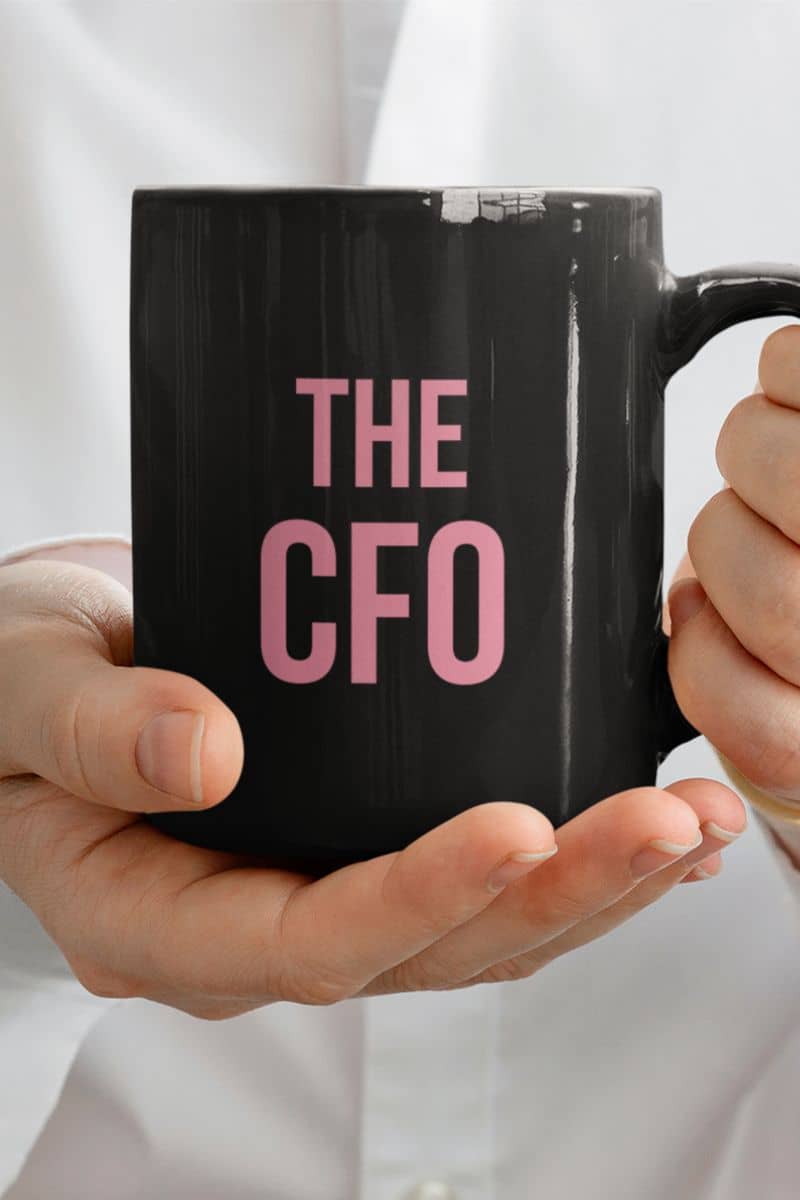 coffee mug gift for female friend with a black mug with 'THE CFO' in pink held by hands against a light background