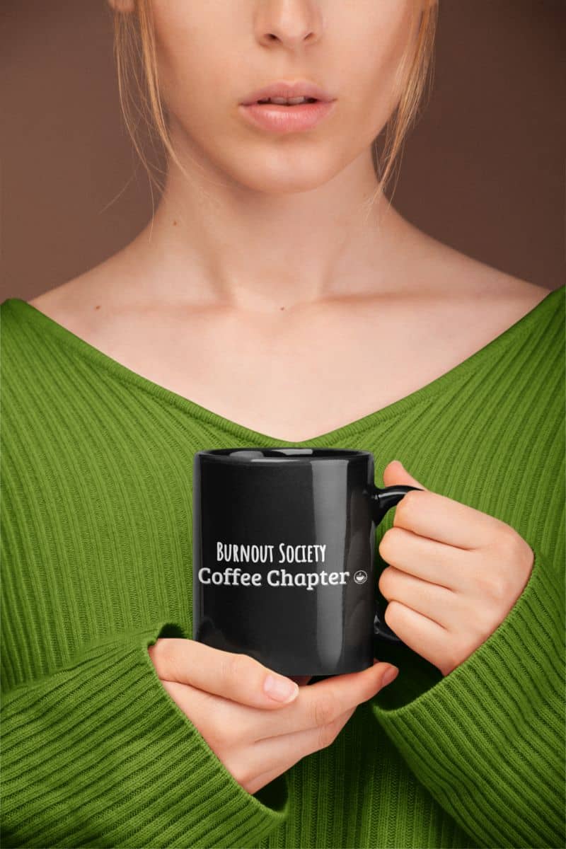 coffee recovery mug with a person holding a black mug with 'Burnout Society Coffee Chapter' text, wearing a green sweater.