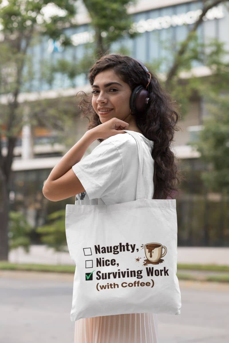 coffee tote bag with a woman holding a tote bag feuturing text 'Naughty, Nice, Surviving Work (with Coffee)' and a coffee cup graphic, outdoors.