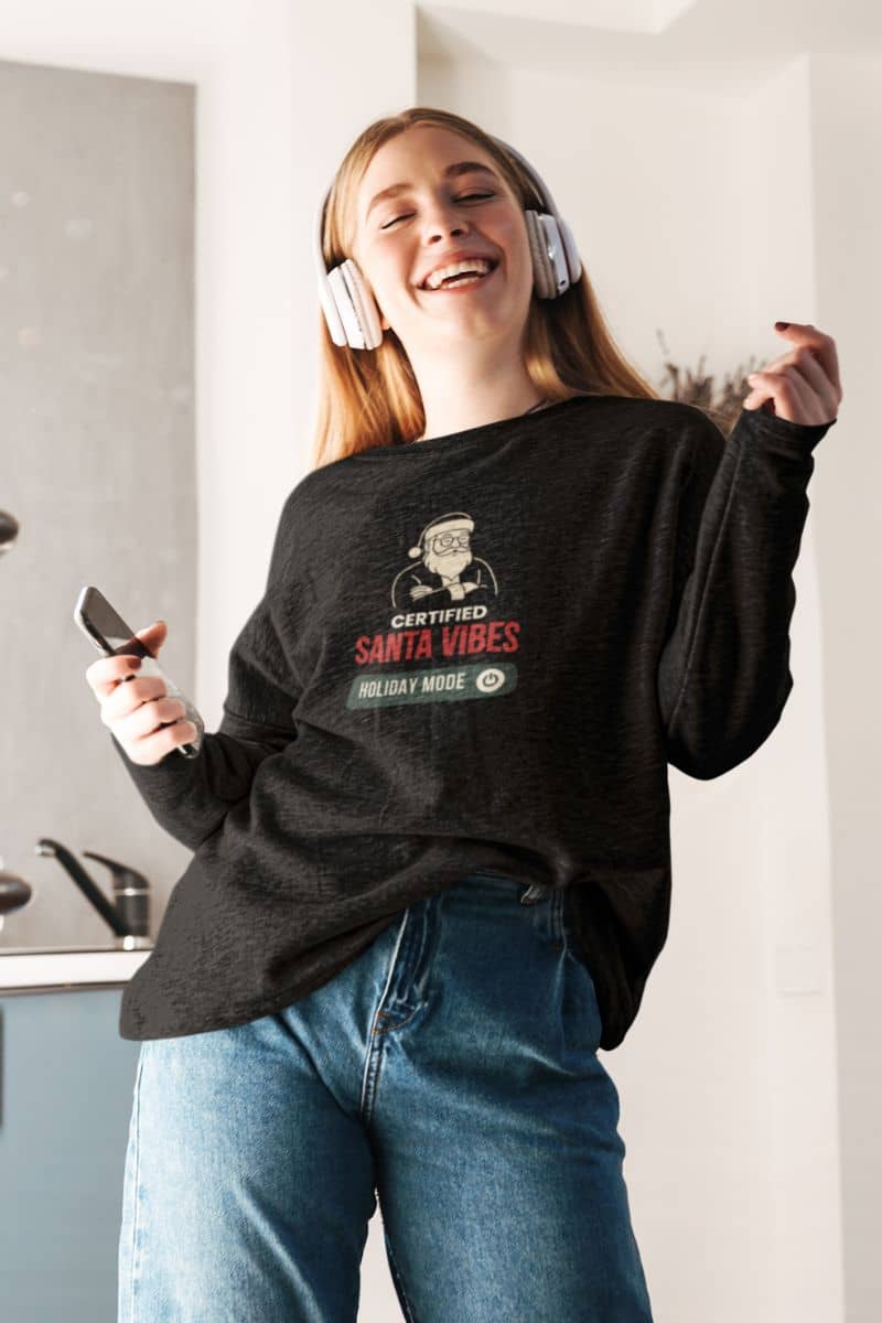 cozy christmas sweater with a person wearing a black sweatshirt with a graphic design, listening to music with headphones, and holding a phone.
