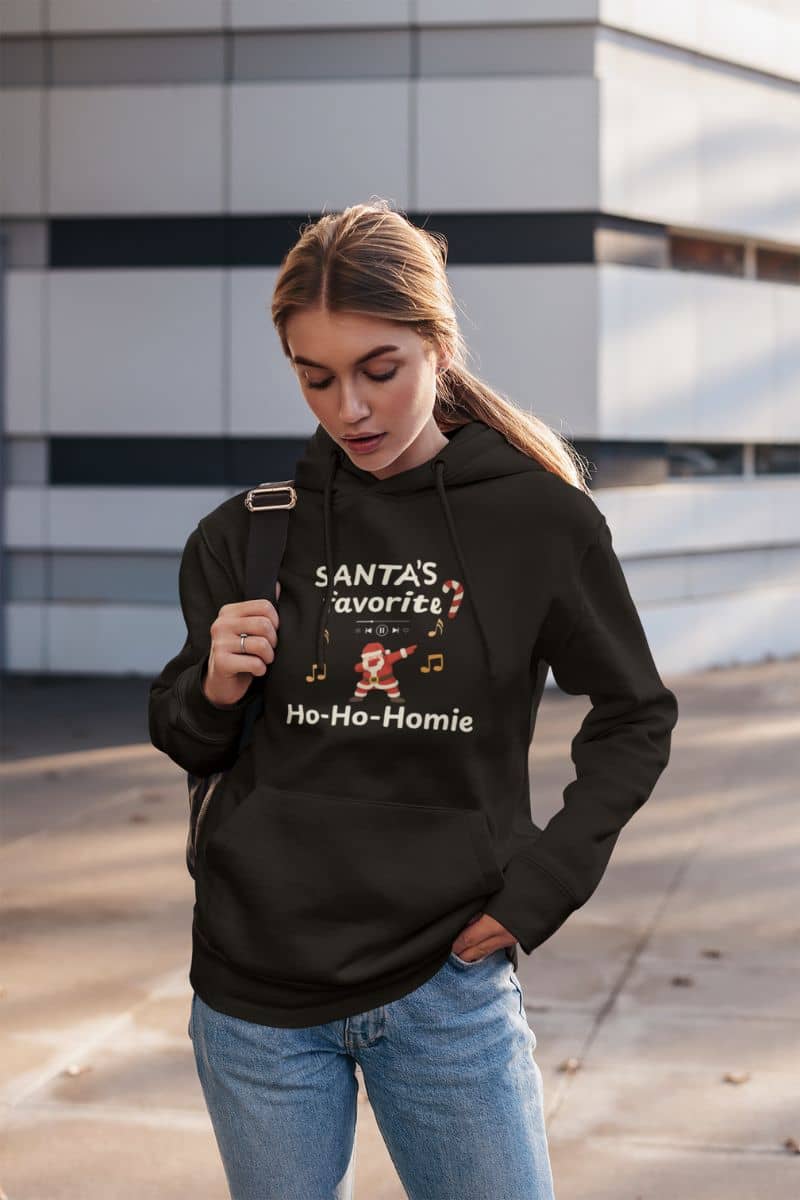 cozy christmas sweatshirt with a woman wearing a black hoodie with text 'Santa's Favorite Ho-Ho-Homie' and graphics, standing outdoors.