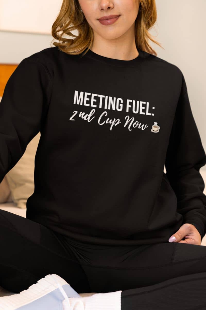 cozy coffee sweatshirt with a person wearing a black sweatshirt with text 'MEETING FUEL: 2nd Cup Now' sitting on a couch.