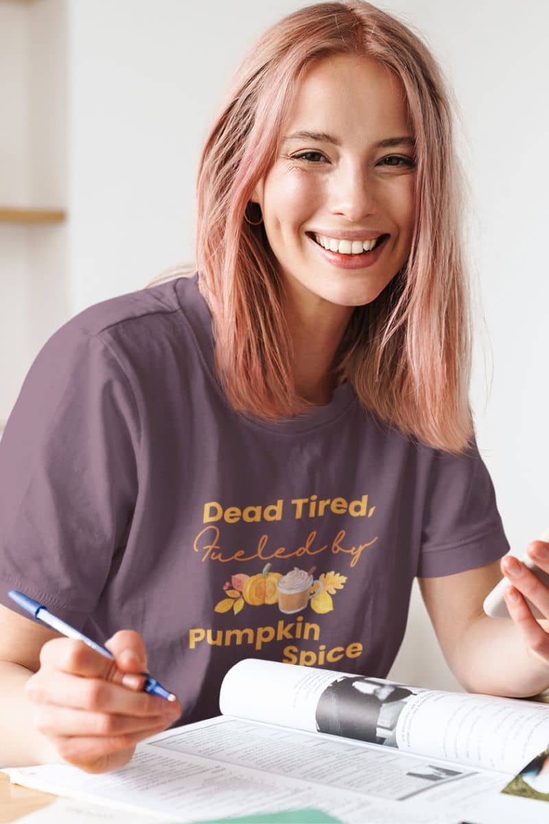 cozy fall outfit showing a woman in a t-shirt with a pumpkin spice-themed design, sitting at a table.