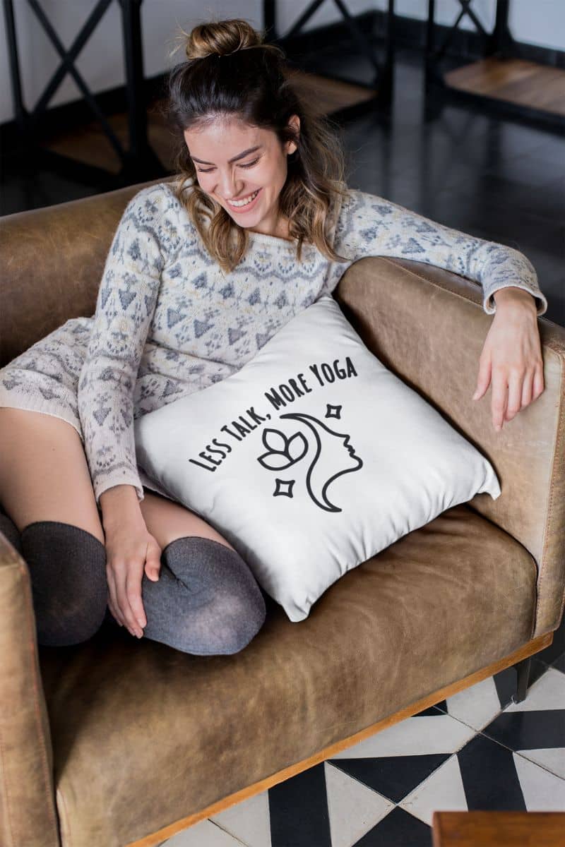 cozy mental health decor with a woman sitting on a couch with a pillow featuring the text 'Less Talk, More Yoga'