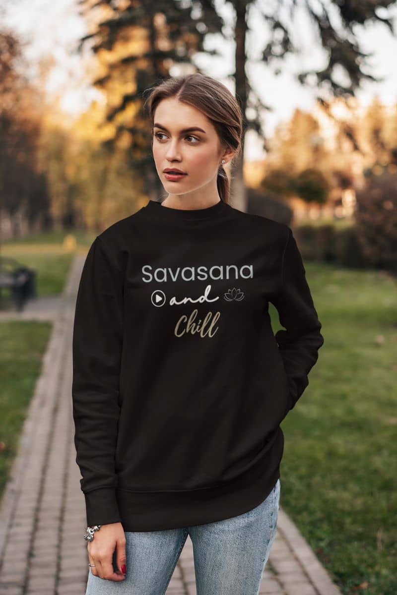 cozy mindfulness sweatshirt with a woman wearing a black sweatshirt with 'Savasana and Chill' text in a park.