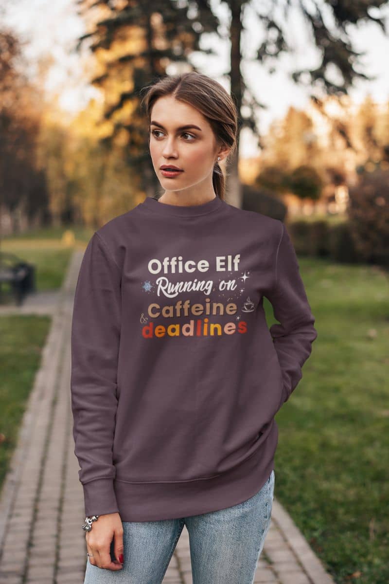 cozy workday sweater with a woman wearing a sweatshirt with text 'Office Elf, Running on Caffeine & Deadlines' in an outdoor setting