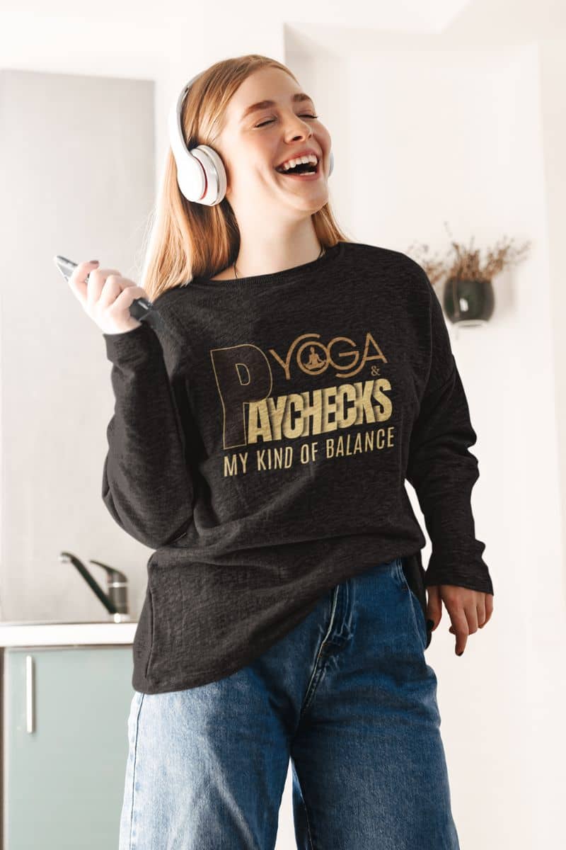 cozy yoga sweatshirt with a person wearing a black sweatshirt with gold text 'Yoga & Paychecks – My Kind of Balance', standing in a kitchen.