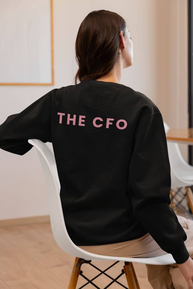 custom couple sweatshirts with a person wearing a black sweatshirt with 'THE CFO' text, sitting on a chair indoors.