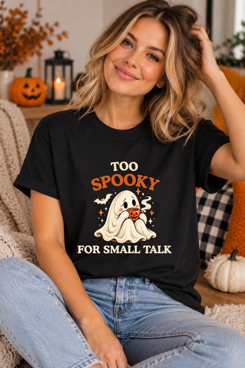 Woman wearing a black cute ghost shirt with the “Too Spooky for Small Talk” design, relaxing on a sofa with Halloween decorations.