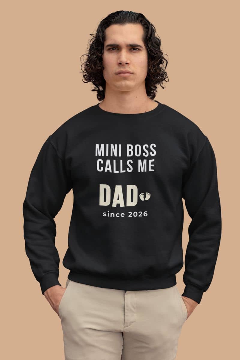 dad life sweatshirt  with a man wearing a black sweatshirt with text 'Mini Boss Calls Me Dad – since 2026' on a beige background 
