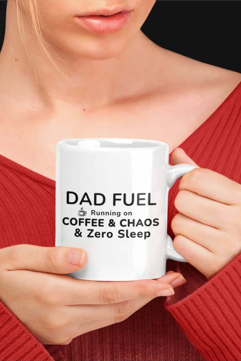 A funny dad mug design featuring a person holding a white mug with the text "DAD FUEL Running on COFFEE & CHAOS & Zero Sleep" against a black background.