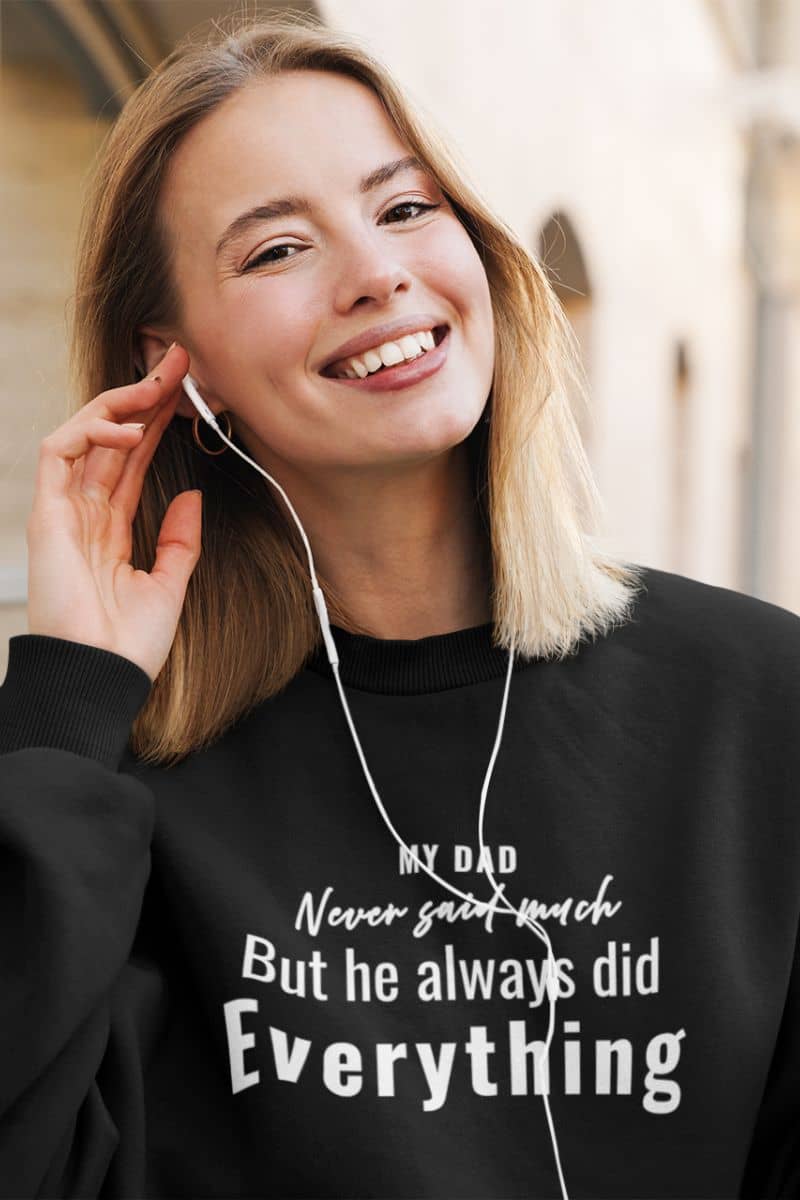 dad sweatshirt with a woman wearing a black sweatshirt with text 'My Dad Never Said Much, He Always Did Everything', listening to music with earphones.