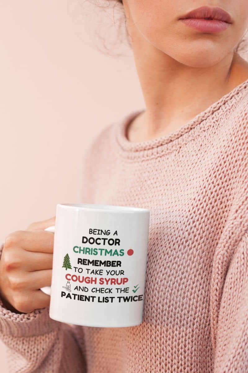 doctor gift mug with a person holding a mug with humorous text 'Being a doctor during Christmas, remember to take your cough syrup and check the patient list twice'