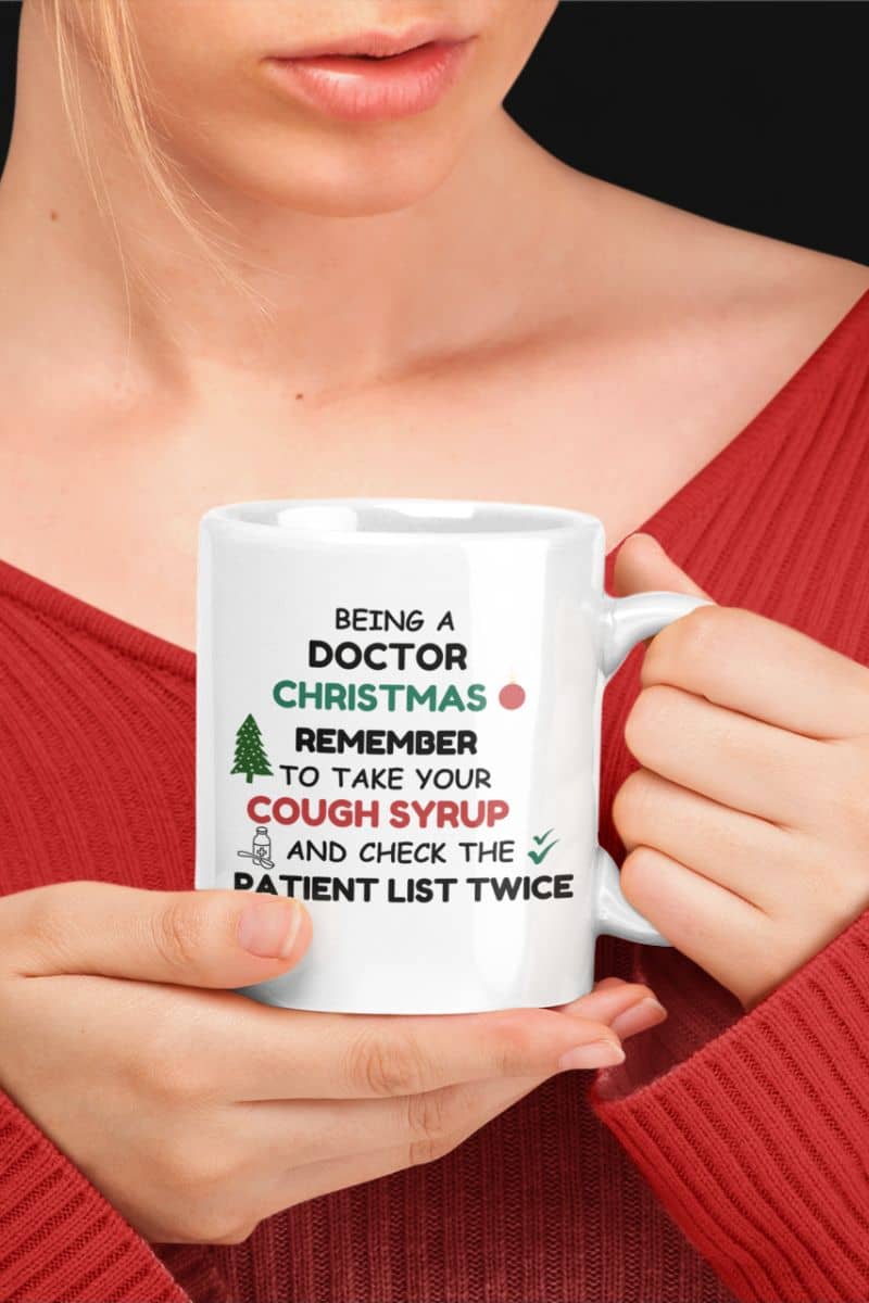 doctor holiday coffee mug with a person holding a mug with text 'Being a doctor during Christmas, remember to take your cough syrup and check the patient list twice' in front of a black background