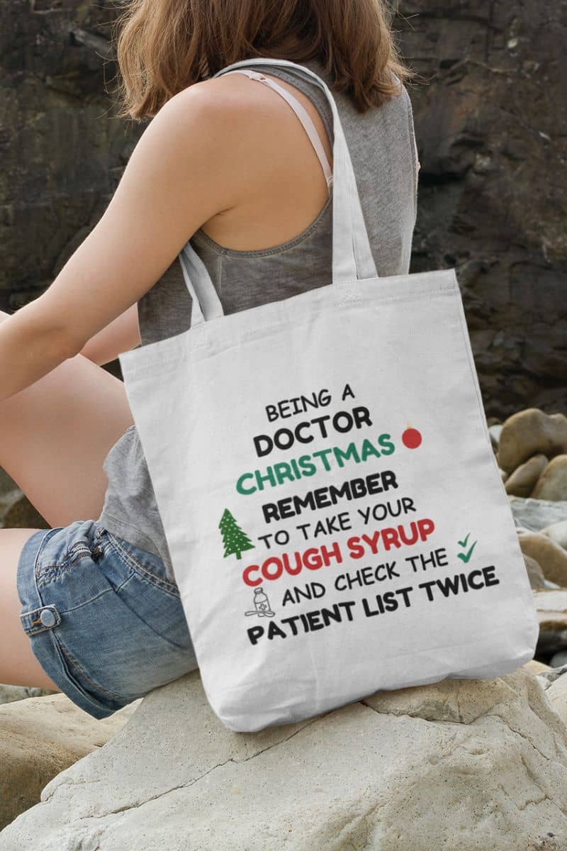 doctor work tote with a person holding a tote bag with text 'Being a doctor during Christmas, remember to take your cough syrup and check the patient list twice'