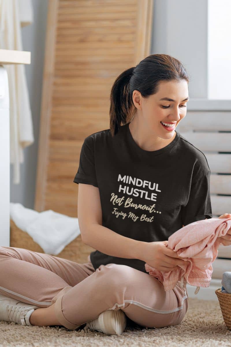 doing my best shirt with a woman sitting on the floor with a 'Mindful Hustle – Not Burnout… Trying My Best' shirt, holding pink fabric.