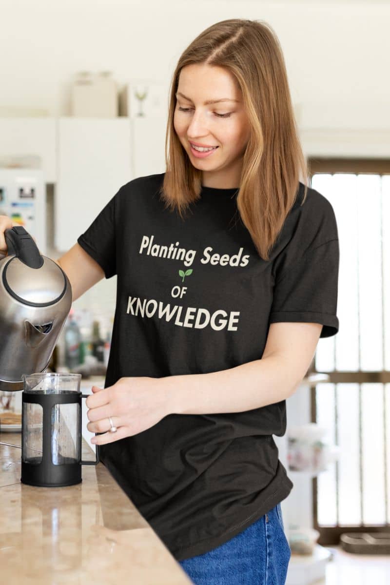 educator shirt with a woman wearing a black t-shirt that reads 'Planting Seeds OF KNOWLEDGE', making coffee in the kitchen