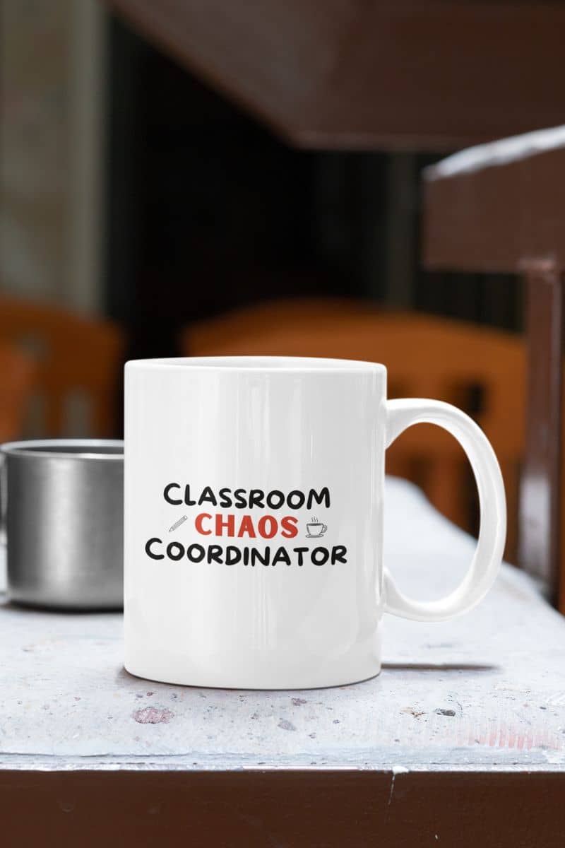 elementary teacher mug with a white ceramic coffee mug with the text 'Classroom Chaos Coordinator' printed on the side, sitting on a table in a classroom setting.