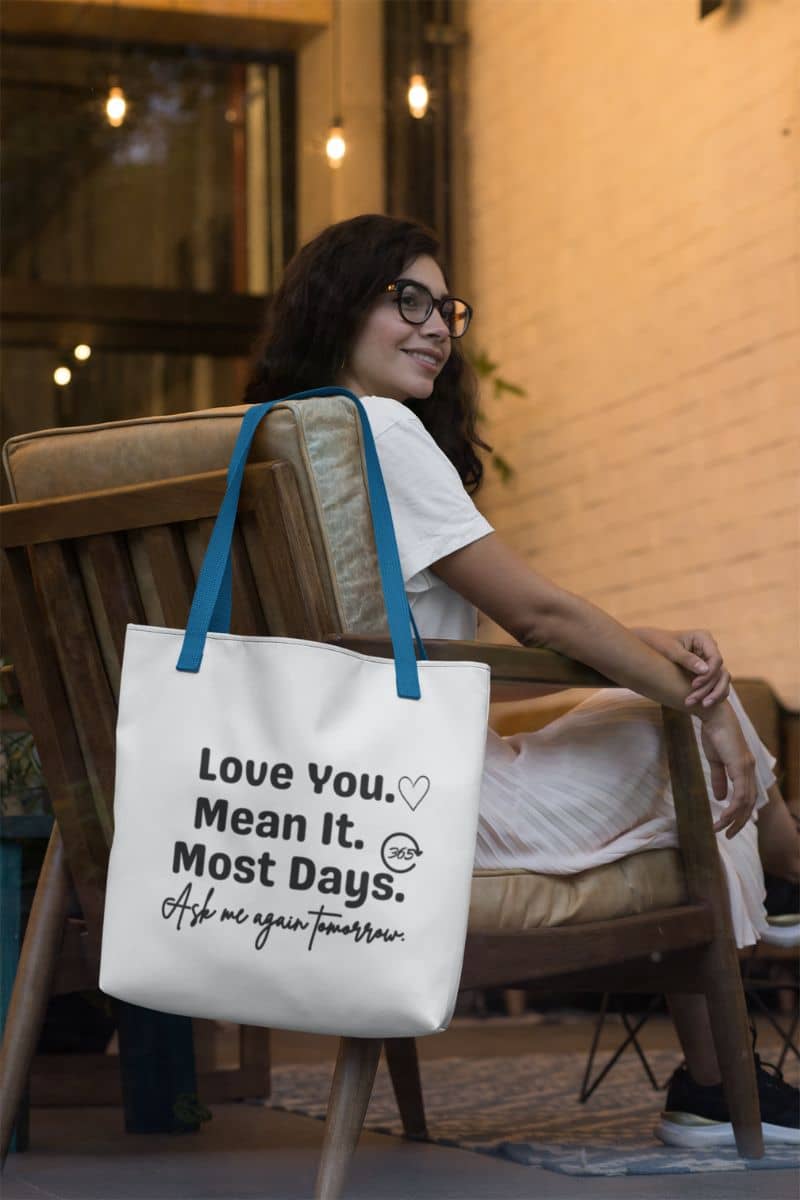everyday couples bag with a woman sitting on a chair with a tote bag featuring text 'Love You. Mean It. Most Days. Ask me again tomorrow.'.