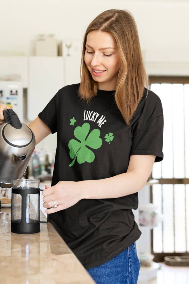 everyday graphic t shirt with a woman in a kitchen wearing a black t-shirt with a green four-leaf clover design and text 'Lucky me.'