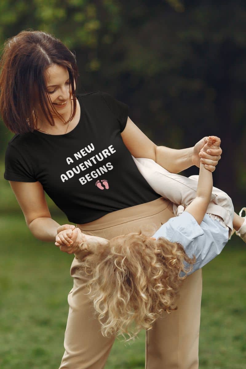 everyday parent t-shirt with a woman holding a child outdoors with a t-shirt that says 'A New Adventure Begins'.