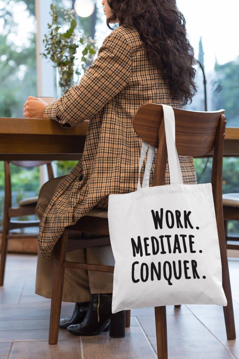everyday work carryall with a person sitting at a table with a tote bag that says 'Work. Meditate. Conquer.'