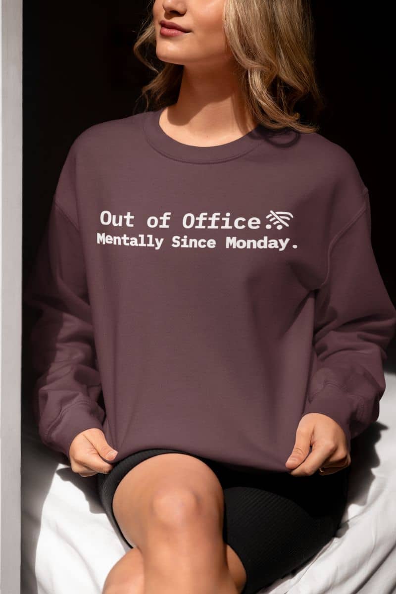 exhausted but present pullover with a person wearing a purple sweatshirt with text 'Out of Office Mentally Since Monday' sitting on a white surface.