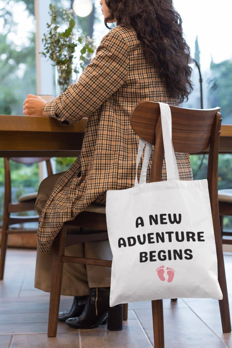 family everyday tote with a person sitting at a table with a tote bag that says 'A New Adventure Begins' in a casual setting.