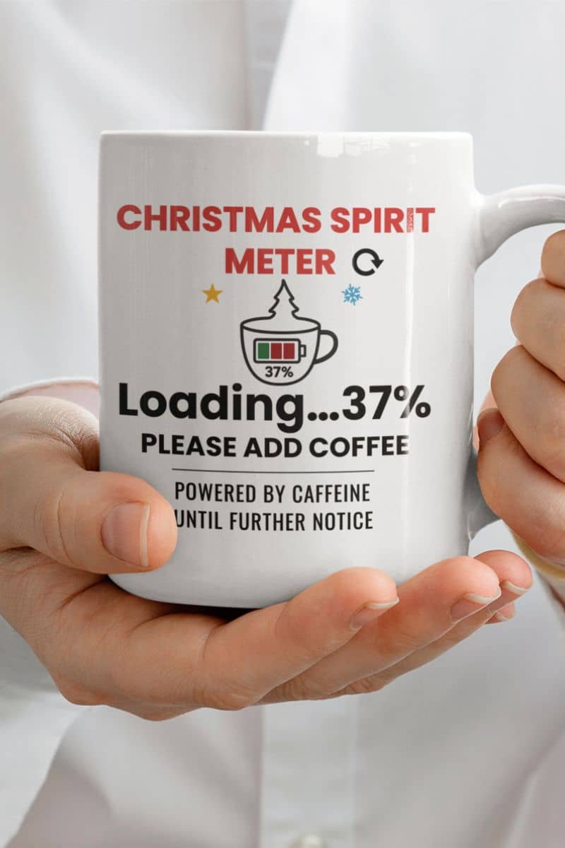 festive coffee cup with a white mug with text 'Christmas Spirit Meter, Loading…37%. Please add coffee. Powered by caffeine until further notice' held by a person