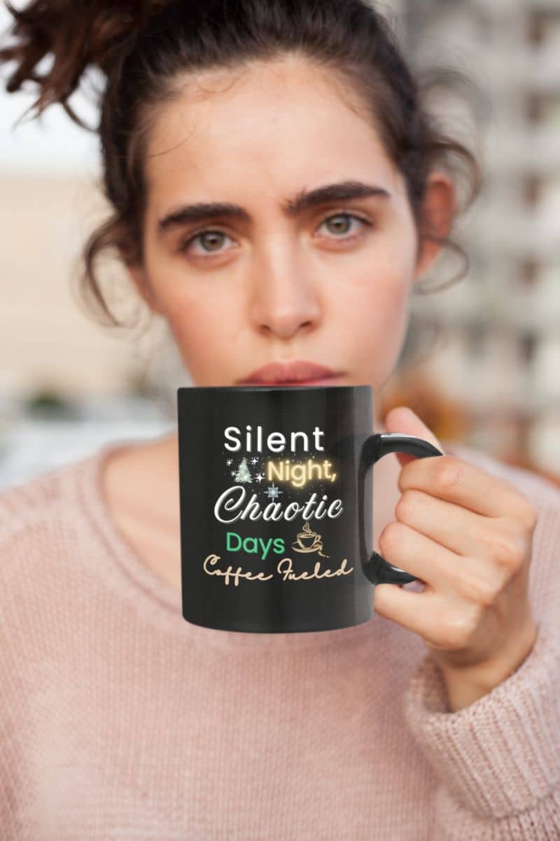 festive coffee cup with a person holding a black mug with text 'Silent Night, Chaotic Days, Coffee Fueled', blurred background