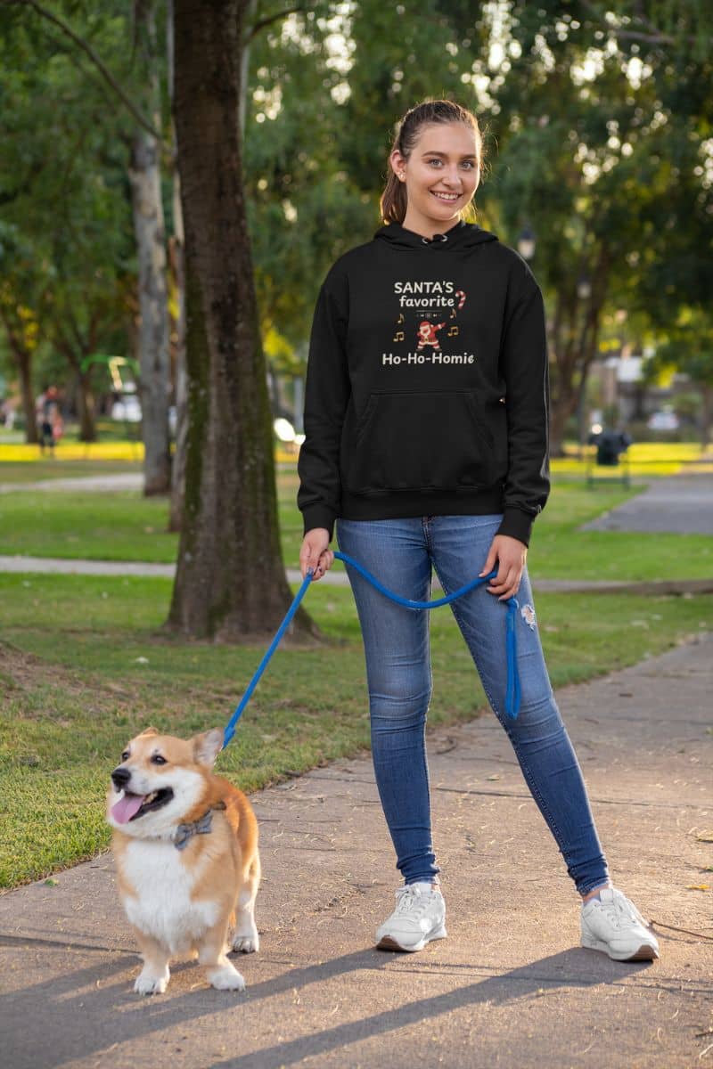 festive fleece hoodie with a woman walking a dog on a leash in a park wearing a black hoodie with text 'Santa's Favorite Ho-Ho-Homie'.