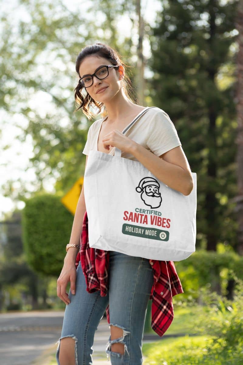 festive minimalist shopper with a woman holding a tote bag with 'Certified Santa Vibes – Holiday Mode On' text outdoors.