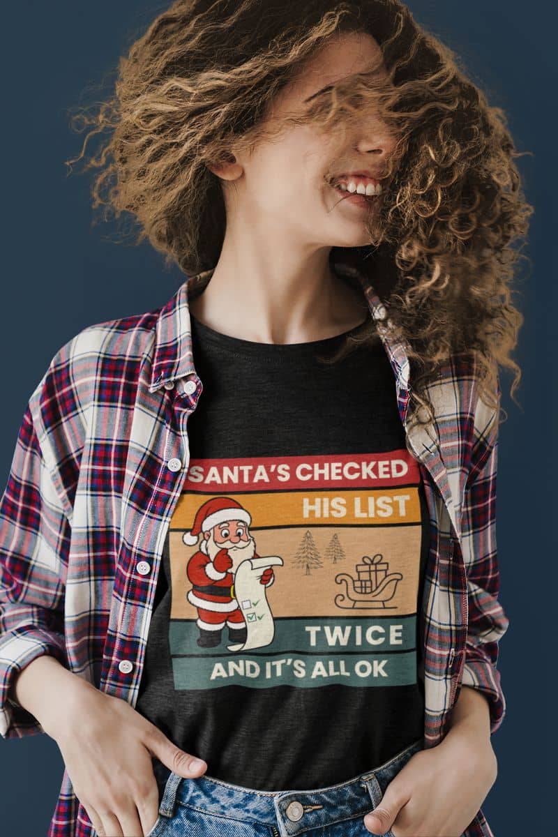 festive party shirt with a person wearing a black t-shirt with text 'Santa's Checked His List Twice And It's All Ok', standing against a dark background.