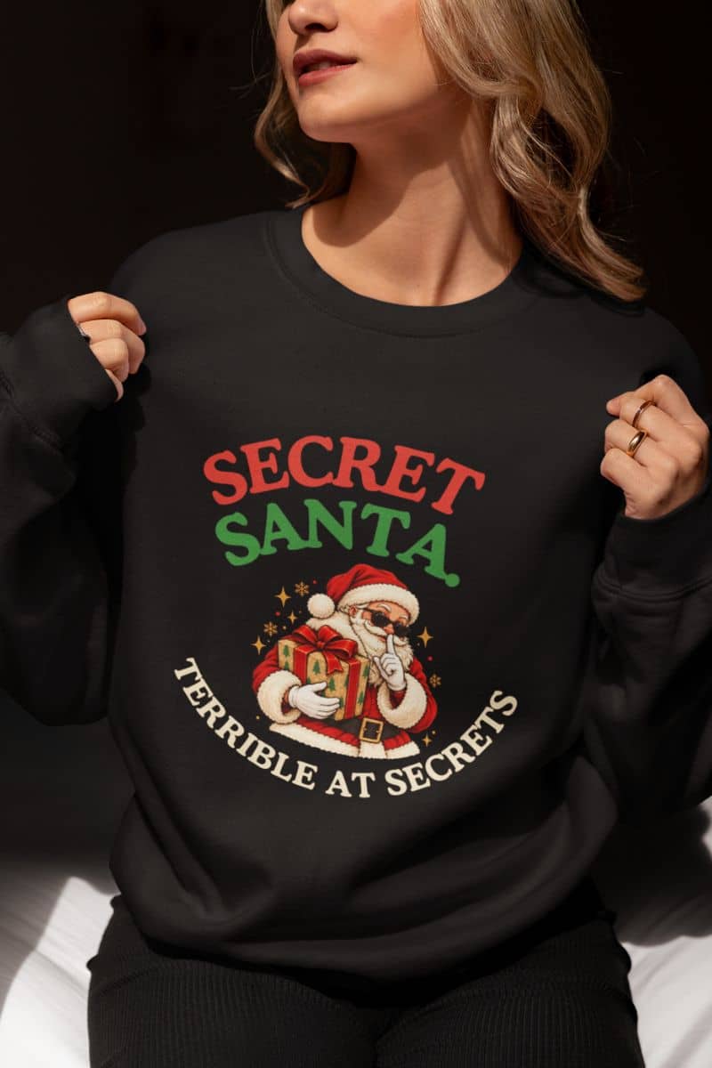 Funny Xmas sweatshirts featuring a Secret Santa Terrible at Secrets design on a black crewneck worn by a woman.