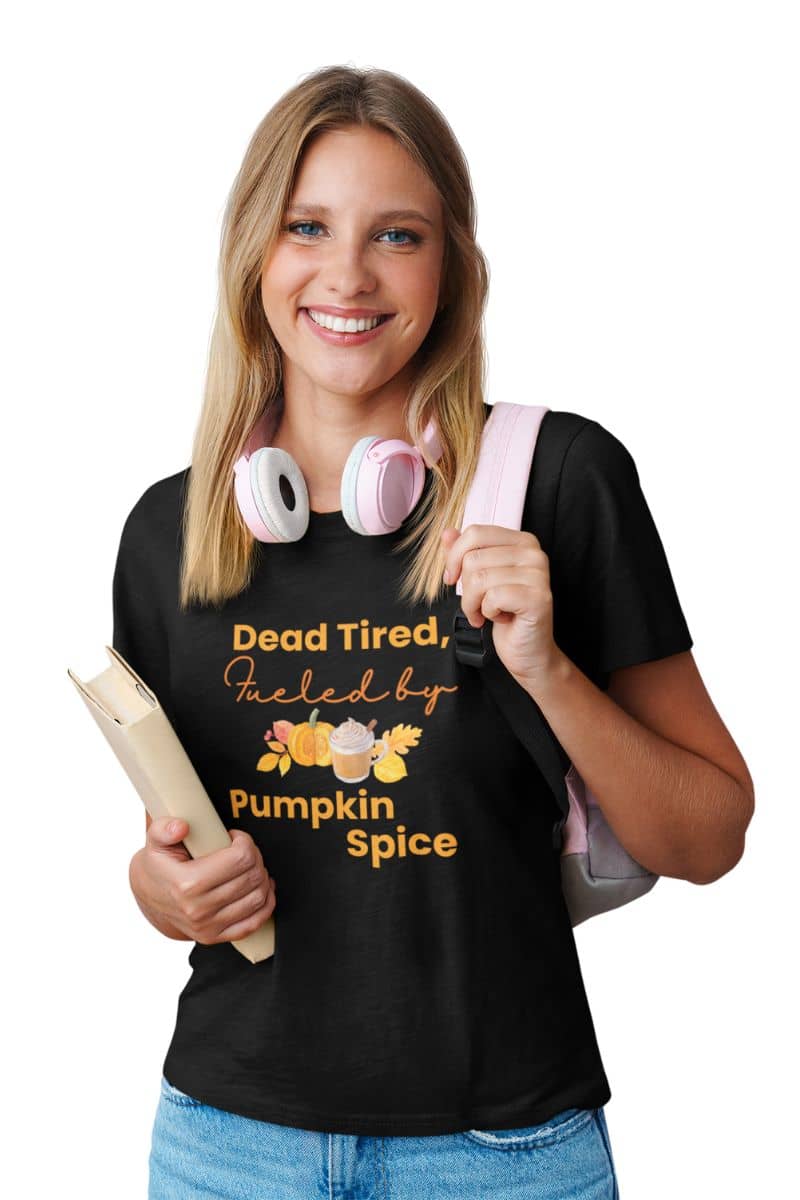 funny autumn tee with a young girl wearing a black t-shirt with text 'Dead Tired, Fueled by Pumpkin Spice', holding books and headphones.