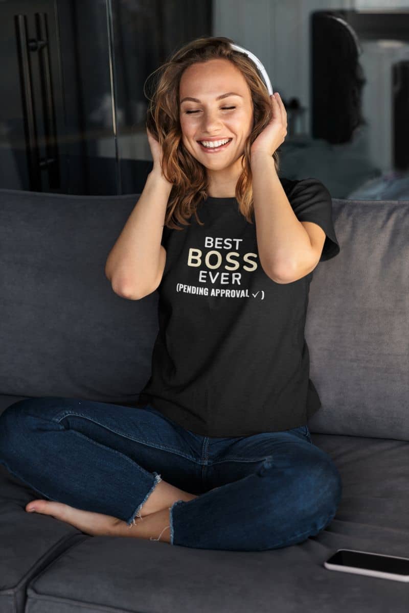 funny boss shirt with a woman wearing a black t-shirt with text 'Best Boss Ever (Pending Approval)' design, sitting on a couch.