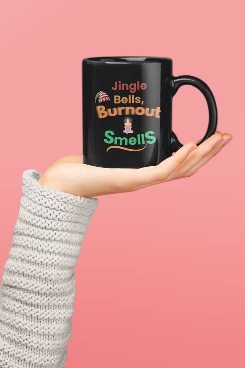 funny burnout mug with a black mug with humorous text 'Jingle Bells, Burnout Smells' held by a person against a pink background