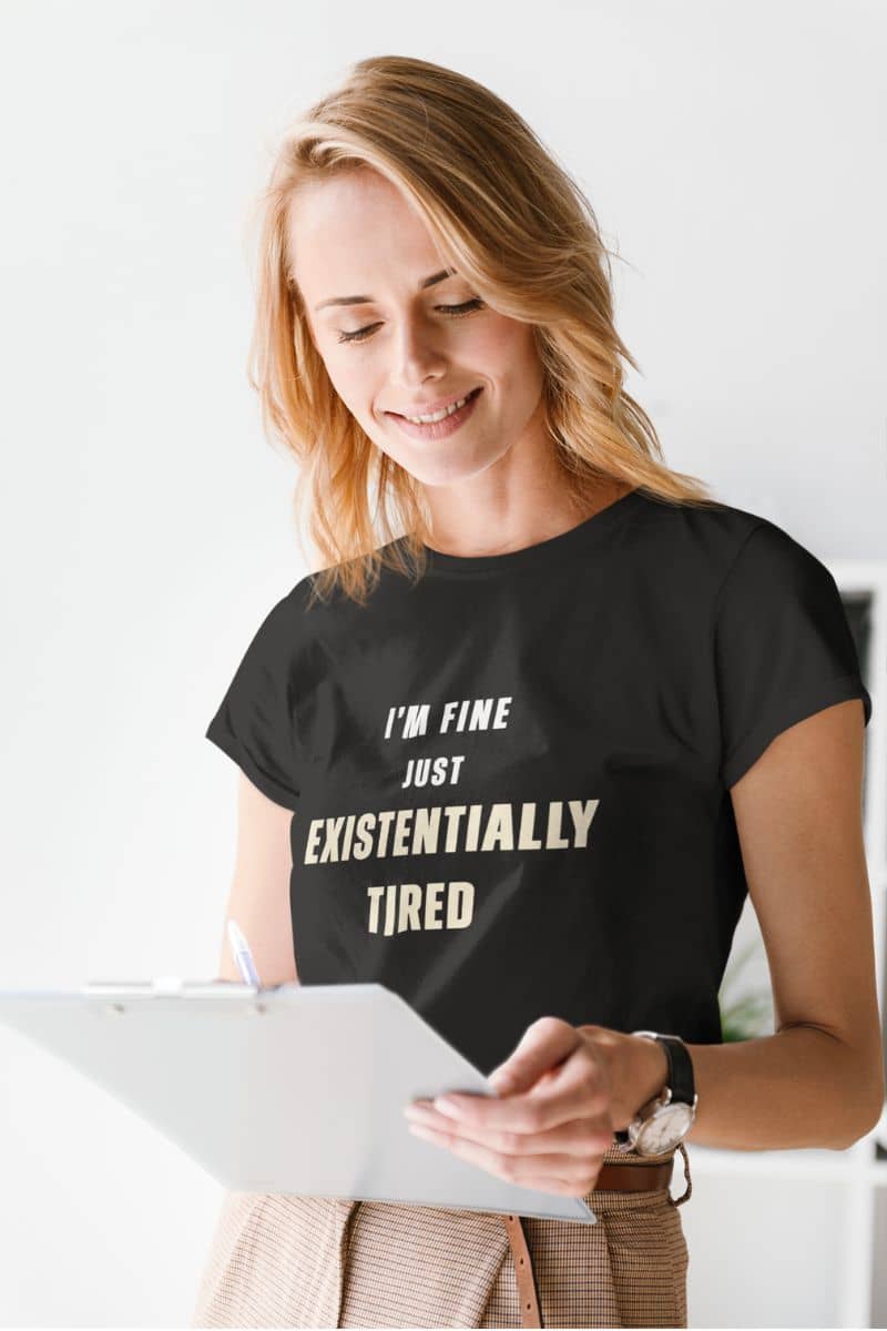 funny burnout shirt with a woman wearing a black t-shirt with text 'I’m fine. Just existentially tired.', holding a tablet.