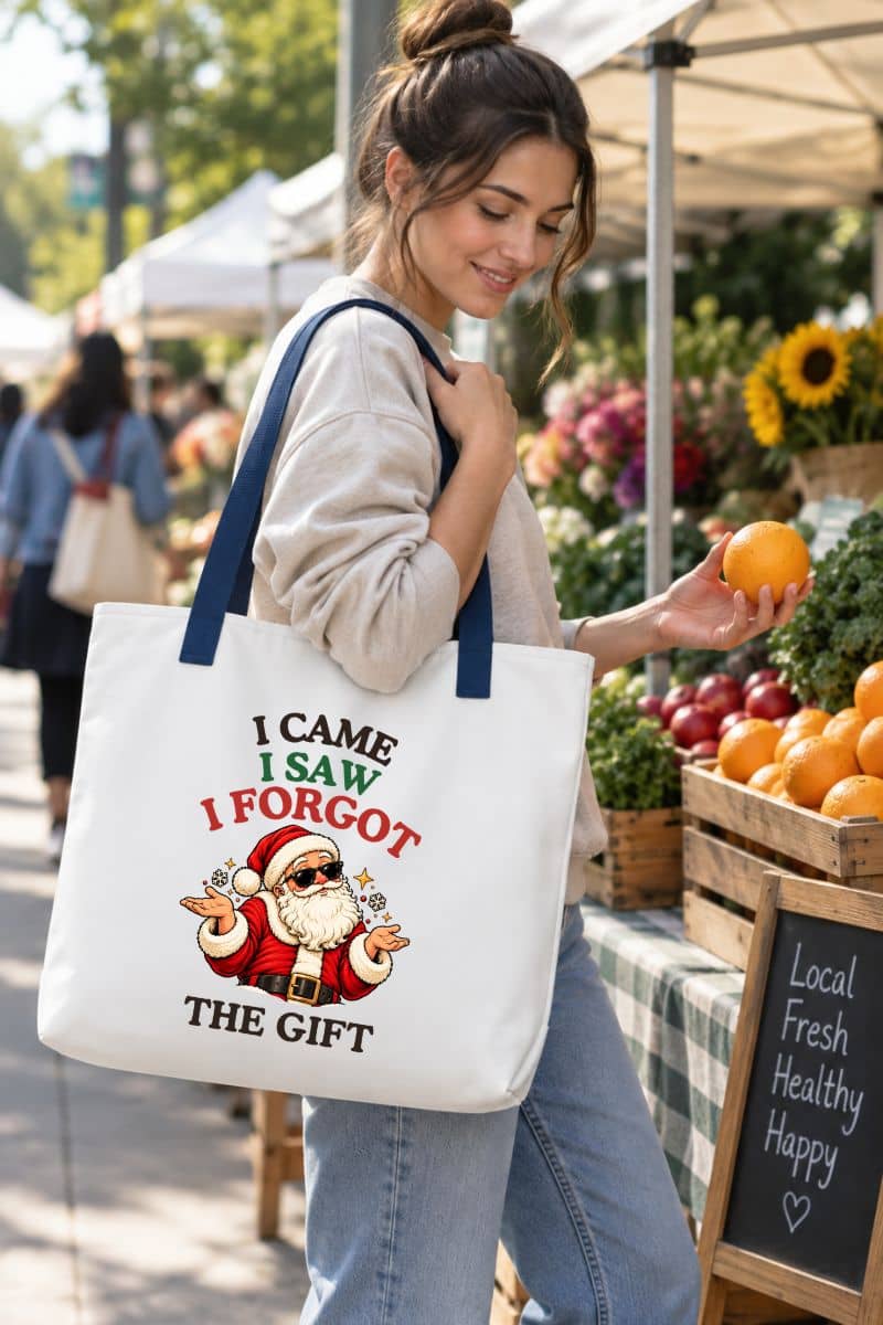 A woman shopping at an outdoor farmers market with a funny Christmas bag featuring a shrugging Santa and “I Came. I Saw. I Forgot the Gift” graphic.