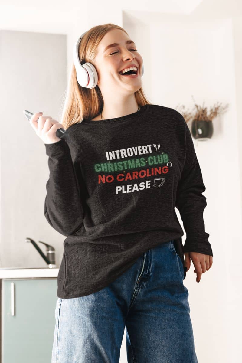 funny christmas sweatshirt with a person wearing a sweater with 'Introvert Christmas Club No Caroling Please' text, standing in a kitchen.