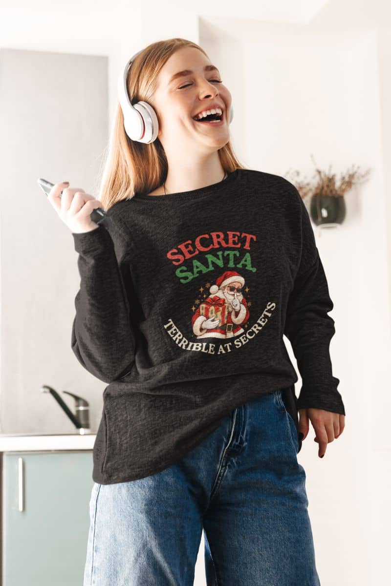 Funny Christmas sweatshirts with a retro Santa holding a gift, modeled by a smiling woman wearing headphones.