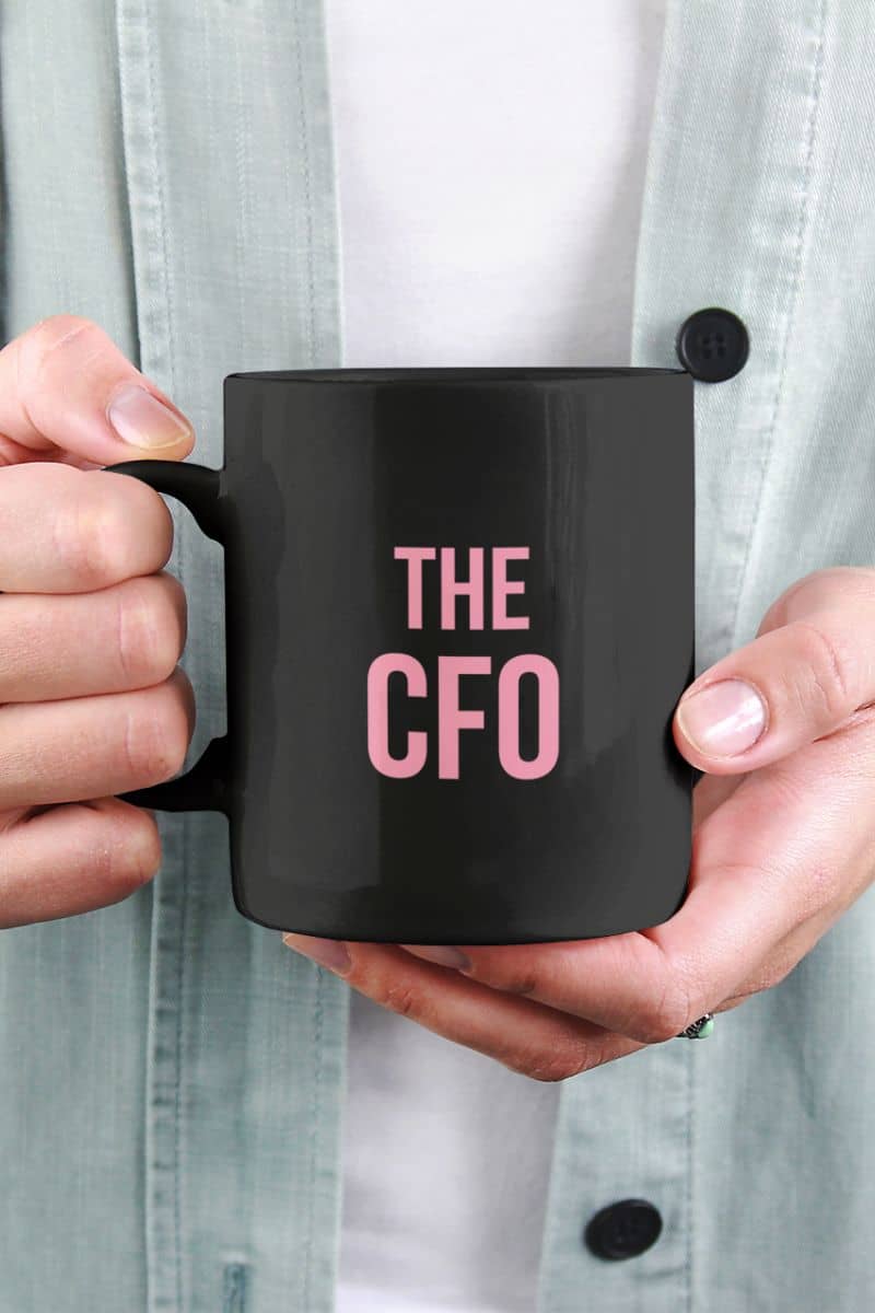 funny coffee mug for wife with a person holding a black mug with 'THE CFO' in pink text.