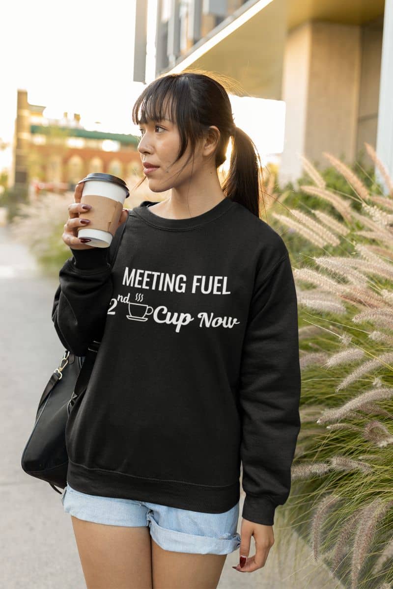 funny coffee sweatshirt with a woman wearing a black sweatshirt with text 'Meeting Fuel: 2nd Cup Now', holding a coffee cup outdoors.
